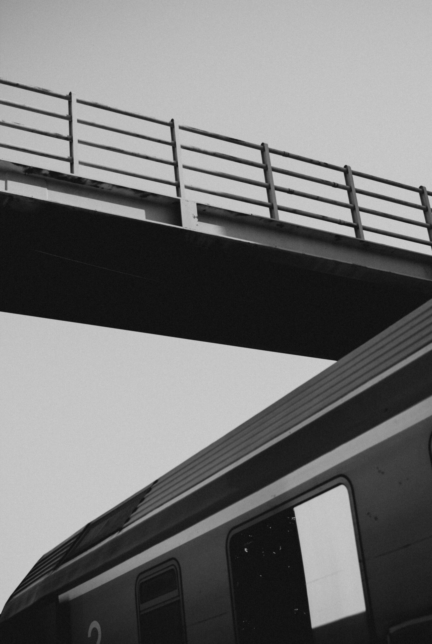 Dramatic black and white view of a train under a footbridge.