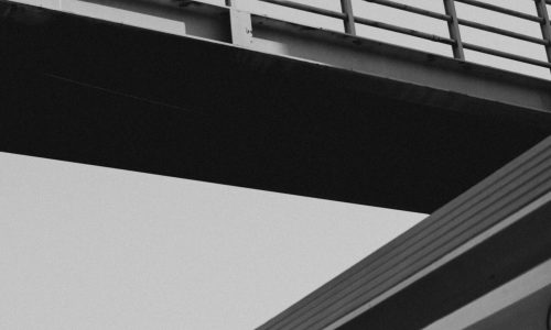 Dramatic black and white view of a train under a footbridge.